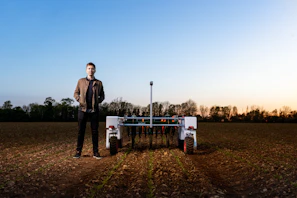 A young farmer using a tablet in the middle of a vast agricultural landscape.
