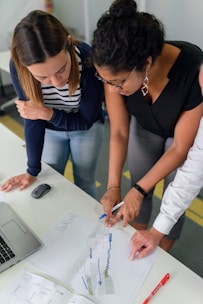 two women leaning over a diagram that they are both working on in a work environment