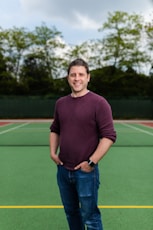 man in maroon crew neck long sleeve shirt and blue denim jeans standing on green field