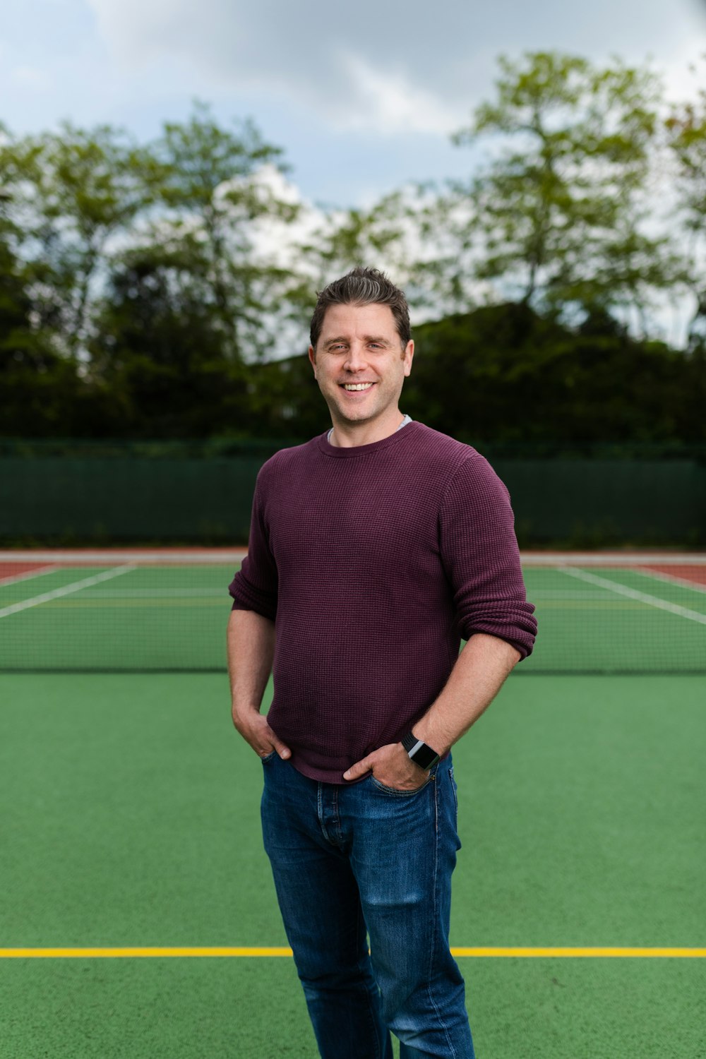 man in maroon crew neck long sleeve shirt and blue denim jeans standing on green field