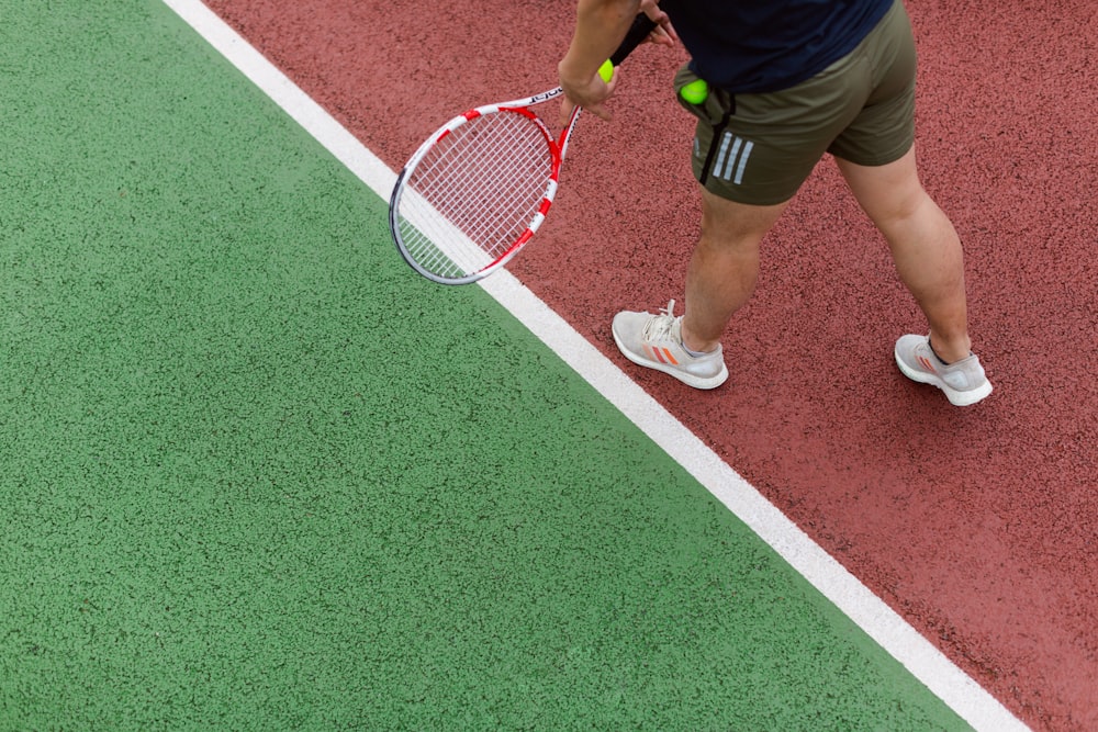 person in black shorts holding red and white tennis racket
