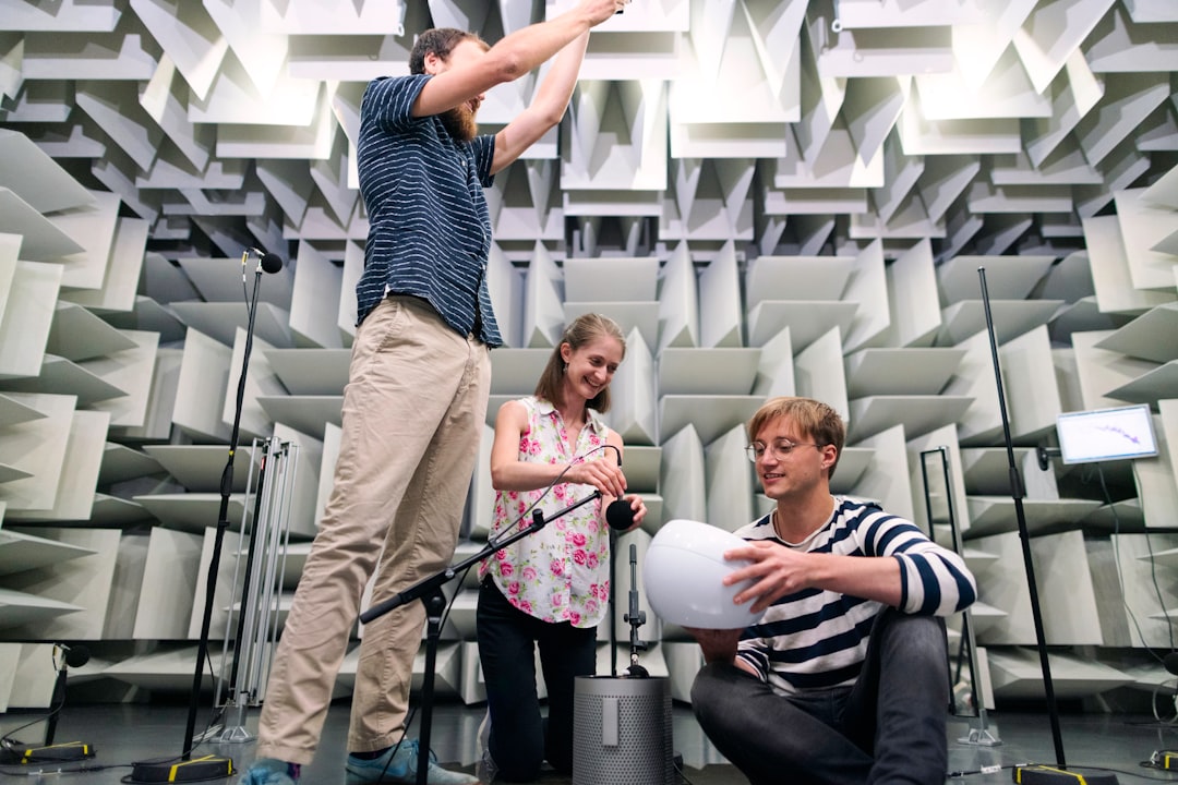 Female noise and vibration engineer sets up microphones to test products with colleagues in anechoic chamber