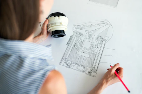 Mechanical engineer reviewing blueprints with a prototype in the background.