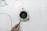 A hand is holding a small device with an attached probe near an electrical fan or turbine surrounded by wires on a clean white surface. The fan is circular with multiple blades, and several wires are connected to it.