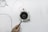 A hand is holding a small device with an attached probe near an electrical fan or turbine surrounded by wires on a clean white surface. The fan is circular with multiple blades, and several wires are connected to it.