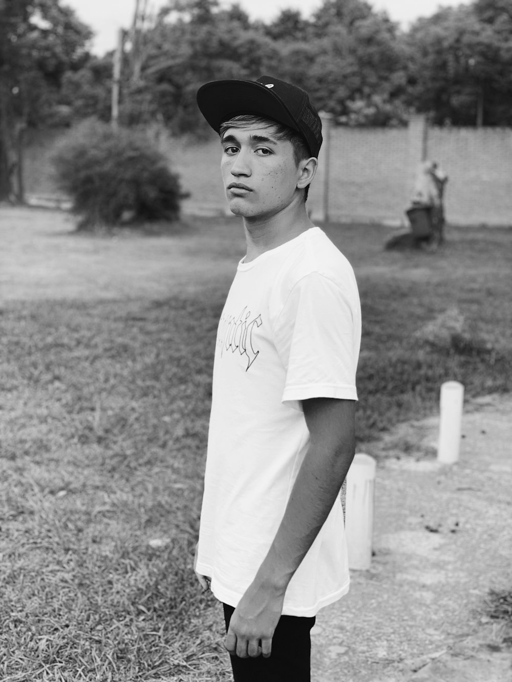 grayscale photo of boy in white crew neck t-shirt and black cap standing on grass