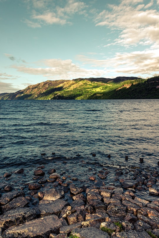 green mountain beside body of water during daytime in Loch Ness United Kingdom