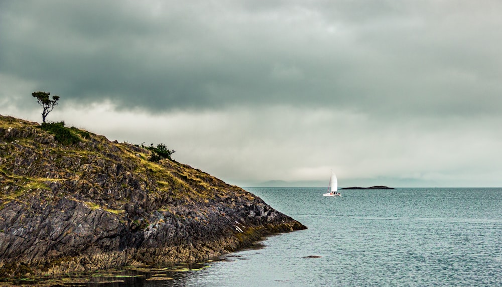 white sailboat on sea near green grass covered hill under white clouds