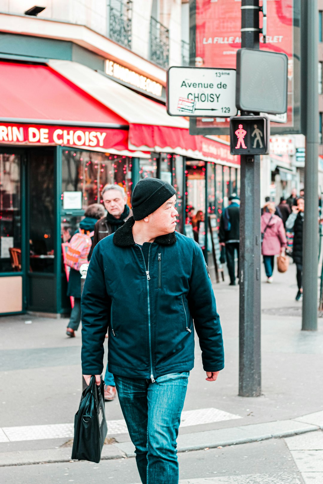 man in red zip up jacket and blue denim jeans walking on sidewalk during daytime