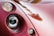 A close-up view of a vintage or classic car's headlight assembly. The image focuses on the curved, glossy red bodywork and the round headlight with a reflective surface. The smoothness and shine of the car's paint suggest it is well-maintained. Lighting creates soft reflections across the surface.