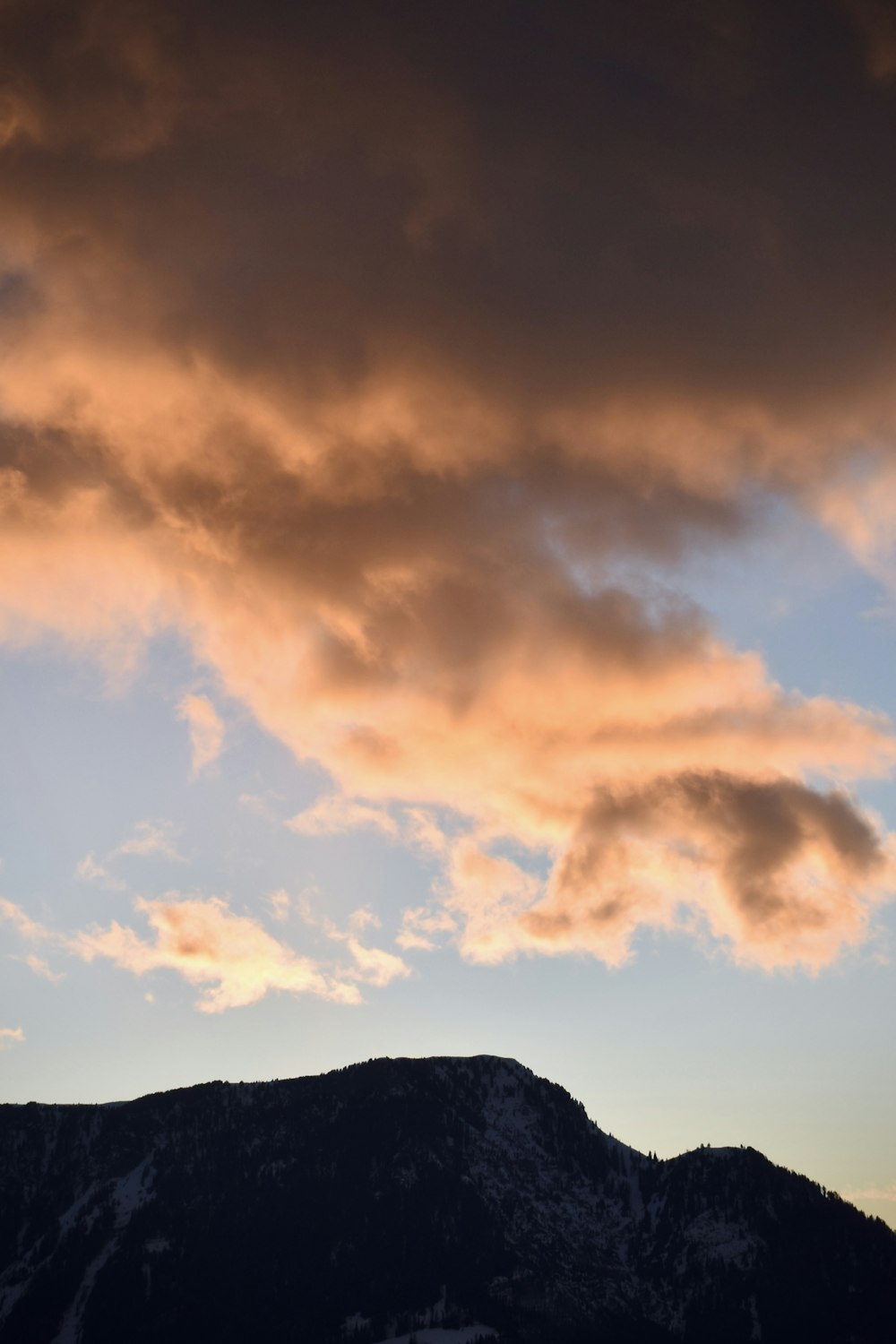 silhouette of mountain under cloudy sky during sunset