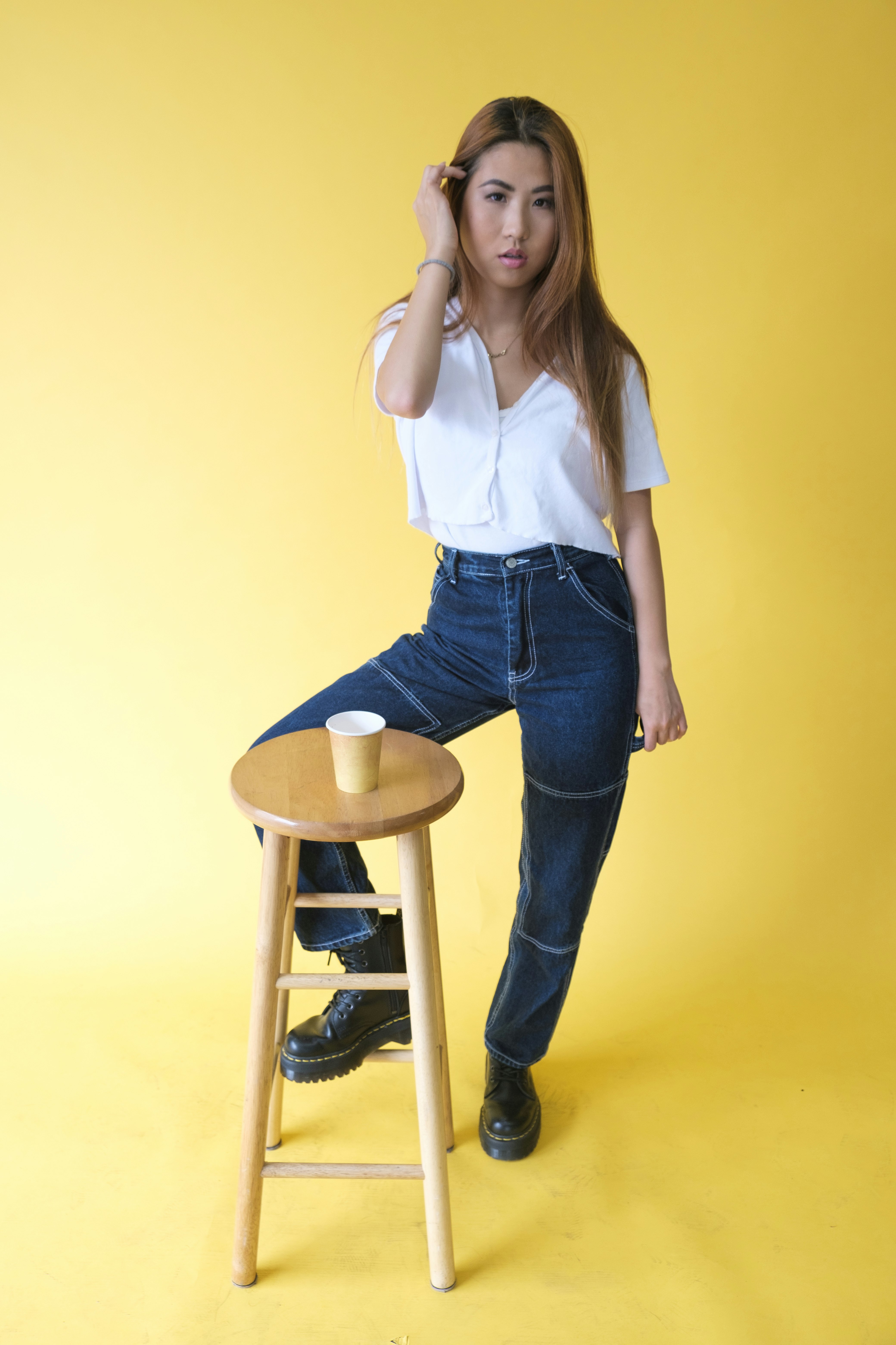 woman in white shirt and blue denim jeans standing beside brown wooden stool