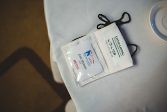 A media badge with a lanyard lying on a white surface. The badge displays the Northern Lights 2020 logo and a name printed below it. Nearby is a partial view of a cup or dish.