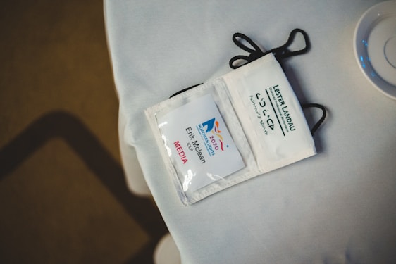 A media badge with a lanyard lying on a white surface. The badge displays the Northern Lights 2020 logo and a name printed below it. Nearby is a partial view of a cup or dish.