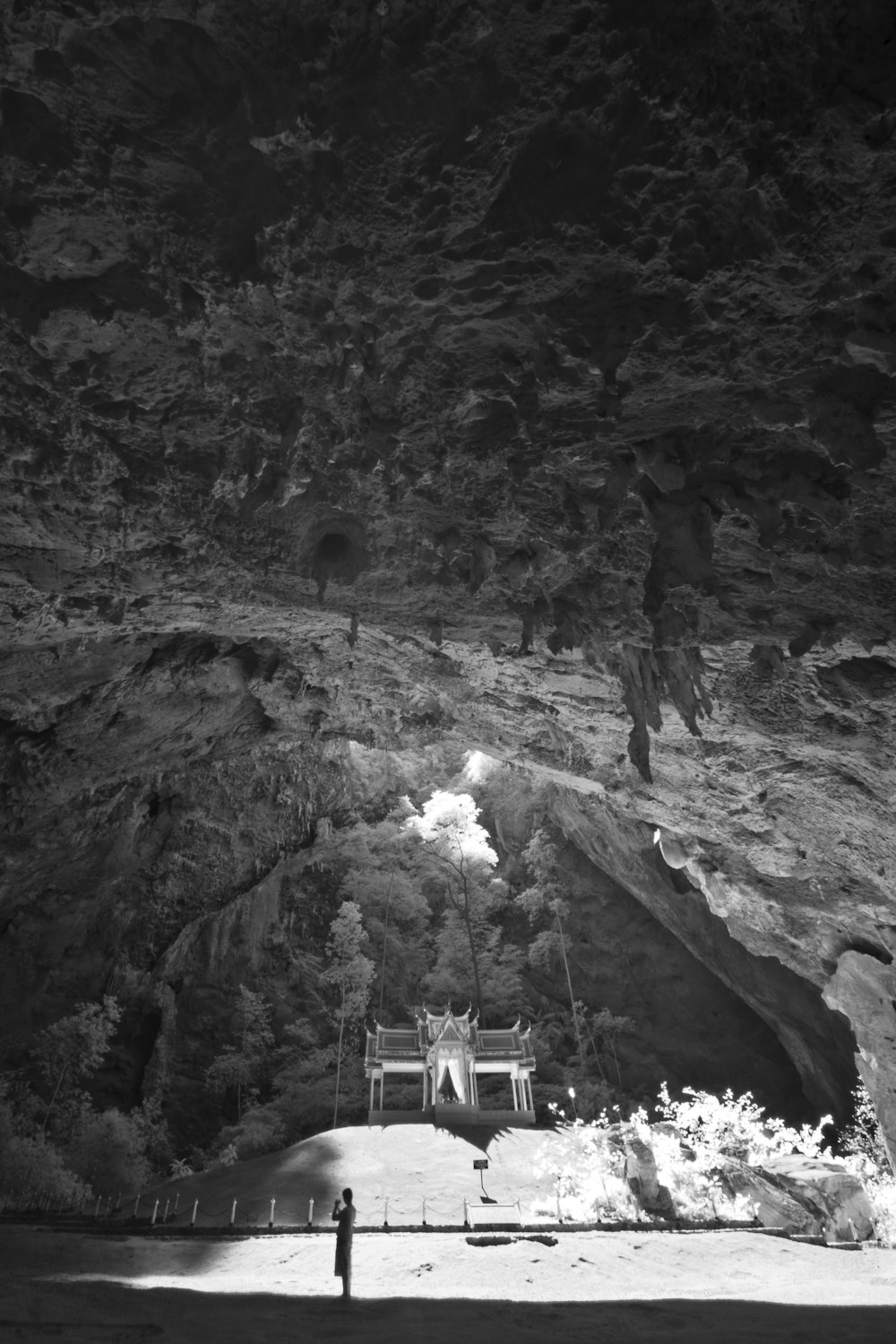 grayscale photo of man standing on rock formation