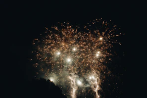 Colorful firecrackers bursting in the sky with vibrant sparks against an evening festival backdrop.