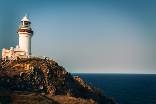white lighthouse on brown rock formation during daytime in Cape Byron State Conservation Area Australia