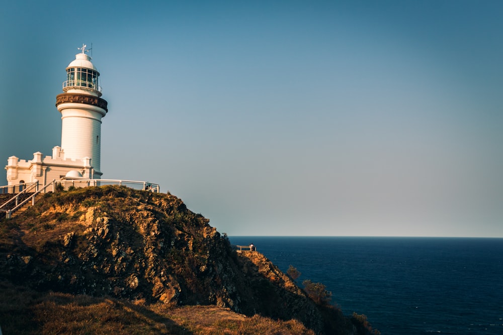 farol branco na formação rochosa marrom durante o dia