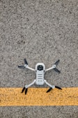 A drone with black propellers is positioned on a textured asphalt surface with a prominent yellow line running horizontally beneath it.