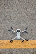 A drone with black propellers is positioned on a textured asphalt surface with a prominent yellow line running horizontally beneath it.