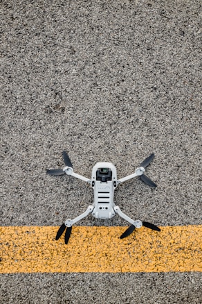 A drone with black propellers is positioned on a textured asphalt surface with a prominent yellow line running horizontally beneath it.