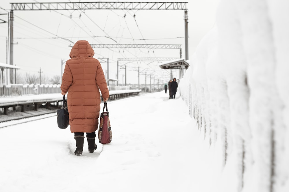 person in orange winter coat walking on snow covered ground during daytime