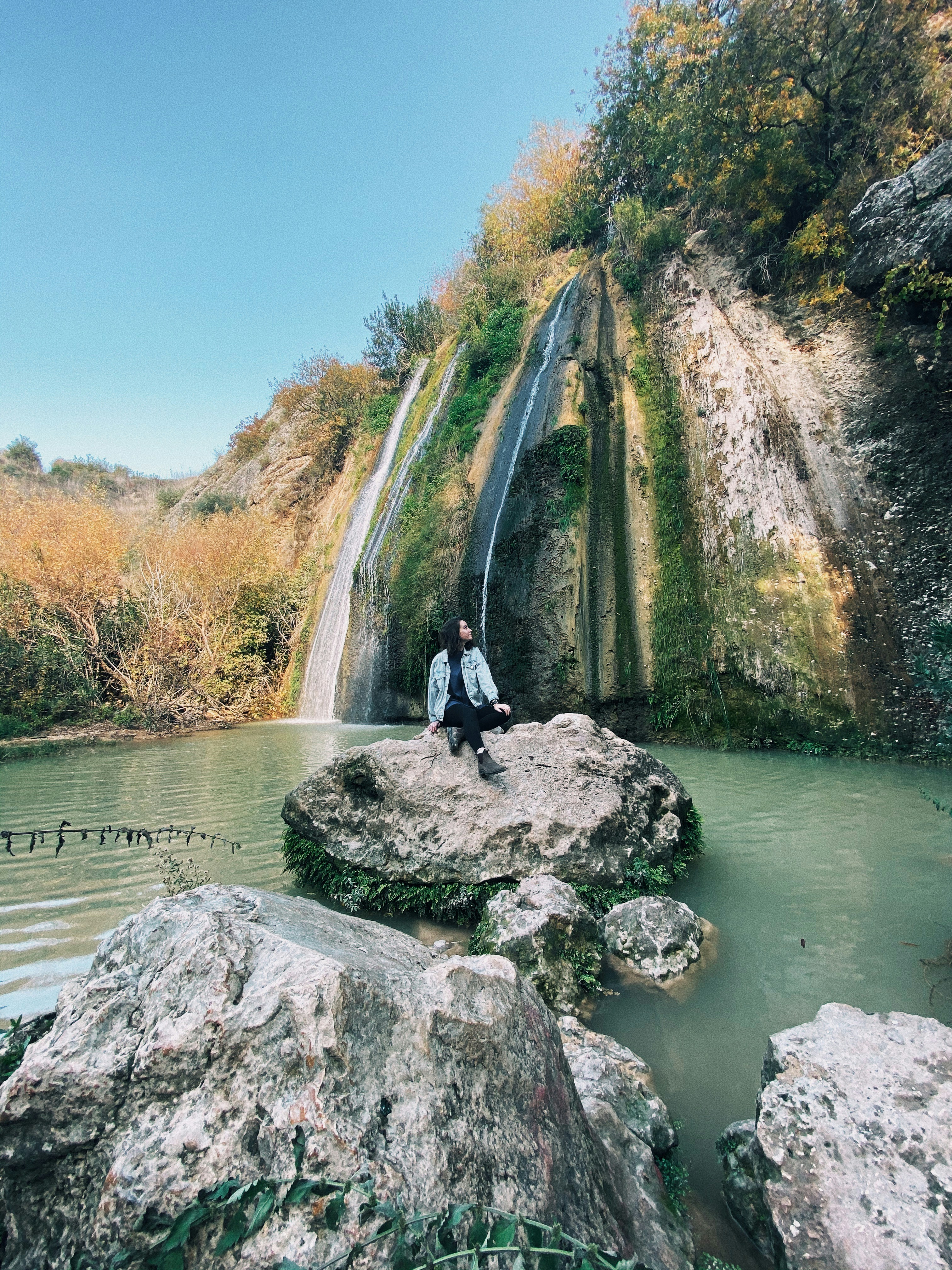 man in black jacket and black pants standing on gray rock near river during daytime