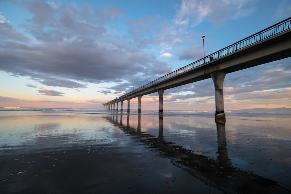 gray concrete bridge over body of water under cloudy sky during daytime