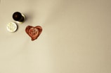 A wax seal with a heart shape and the words 'with love' is stamped on a light-colored surface. A handle, likely part of a seal stamp, rests nearby along with the metal stamp component showing the inverted phrase.