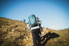 man in blue jacket and black pants with blue backpack walking on brown field during daytime
