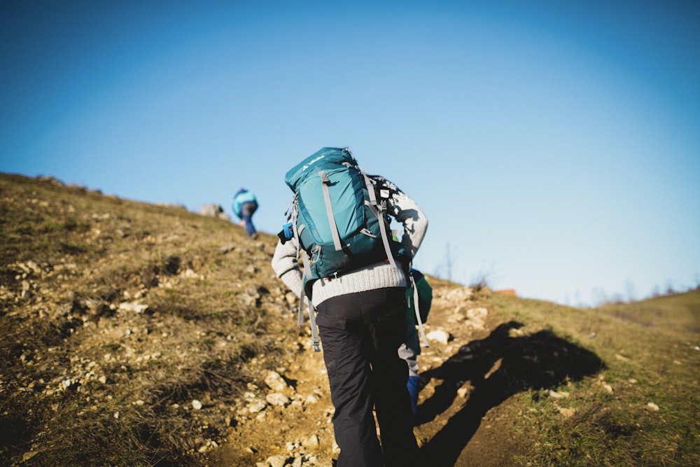 man in blue jacket and black pants with blue backpack walking on brown field during daytime