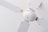 A close-up view of a white ceiling fan with four blades. The fan is mounted on the ceiling with a minimalistic design, featuring metallic screws at the base of each blade. The white color of the fan blends into the ceiling, providing a clean and simple aesthetic.