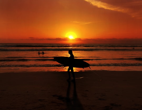 silhouette of man holding surfboard walking on beach during sunset in Kuta Indonesia