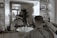 A man is getting a haircut in a barbershop. The scene is reflected in a large mirror that also shows various grooming products on the counter. The barber is standing behind the man, using a clipper and a comb. The ambiance is vintage with tiled walls and a framed photo on a shelf.