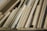 A collection of wooden planks and boards of various sizes, textures, and shades are stacked vertically. The surfaces show grains and patterns typical of wood, ranging from light to medium brown colors. Some boards appear to be plywood, while others might be solid wood pieces.