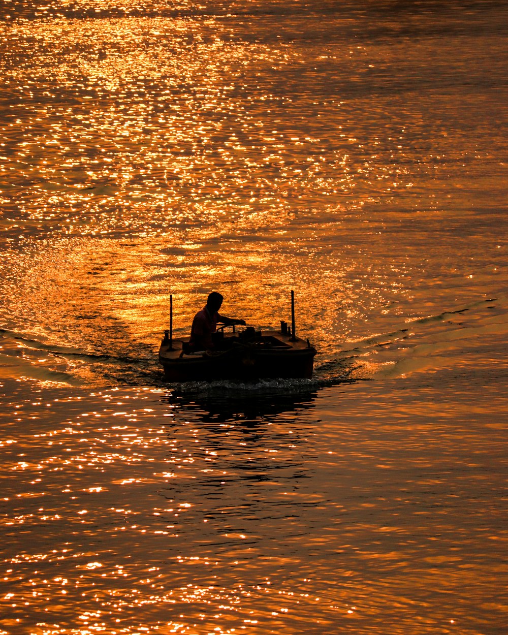 silhouette of 2 people riding on boat on body of water during sunset