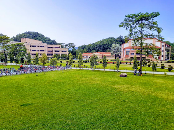 Students collaborating on a campus lawn with modern academic buildings in the background.