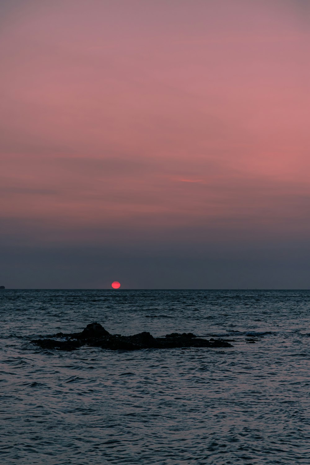 silhouette of rocks on sea during sunset