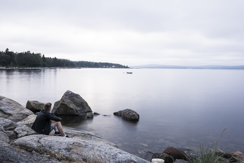 homme et femme assis sur un rocher près d’un plan d’eau pendant la journée