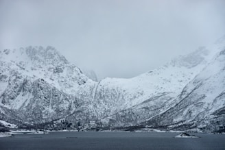 snow covered mountain near body of water during daytime