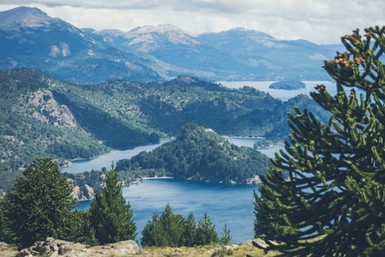 green trees near lake and mountains during daytime in Villa Pehuenia Argentina