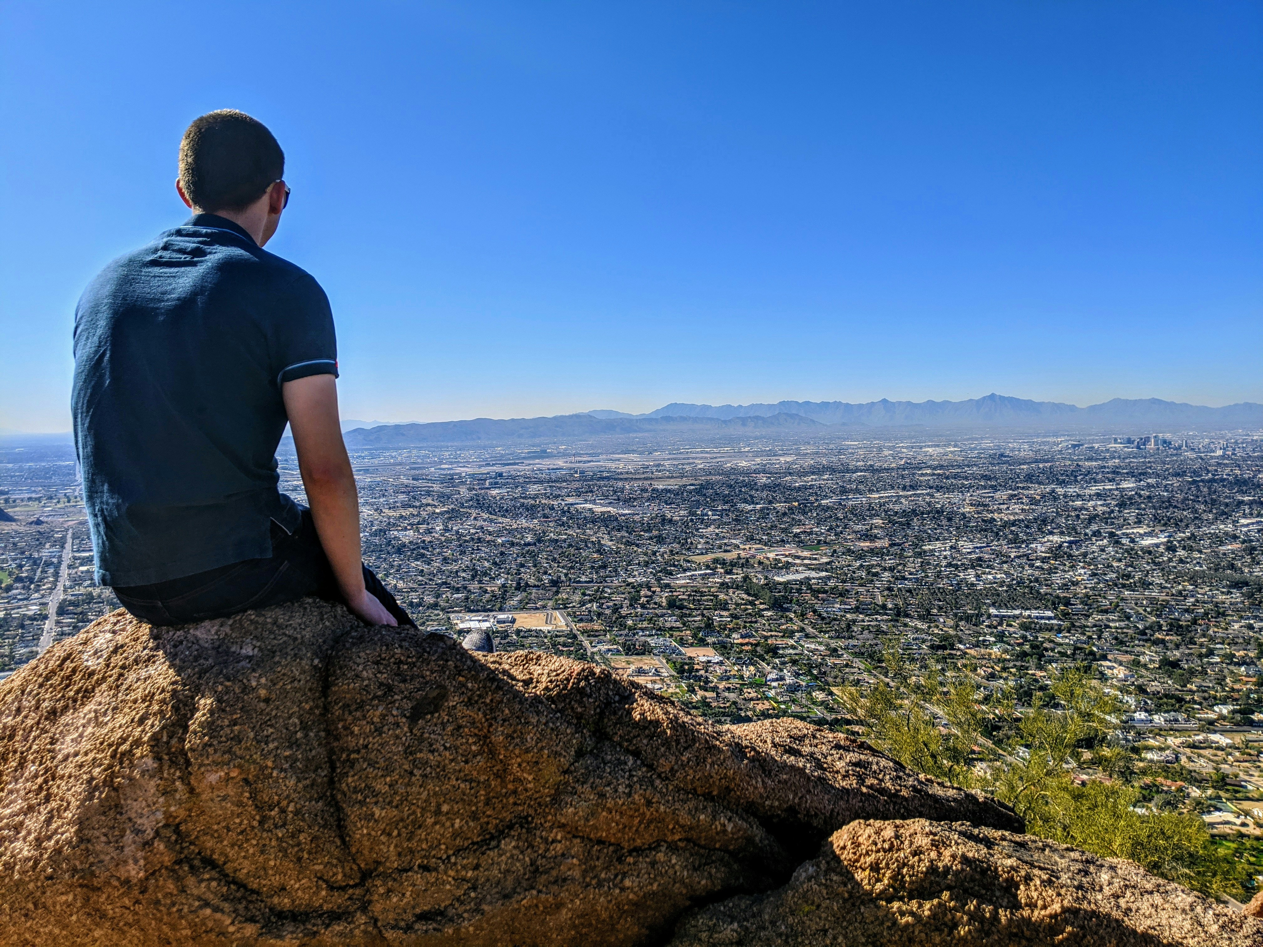 Mann im grauen T-Shirt sitzt tagsüber auf braunem Felsen