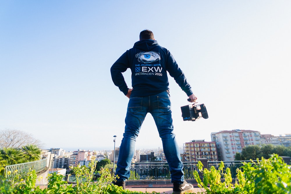 homem em jaqueta azul e preta e jeans azul segurando smartphone preto