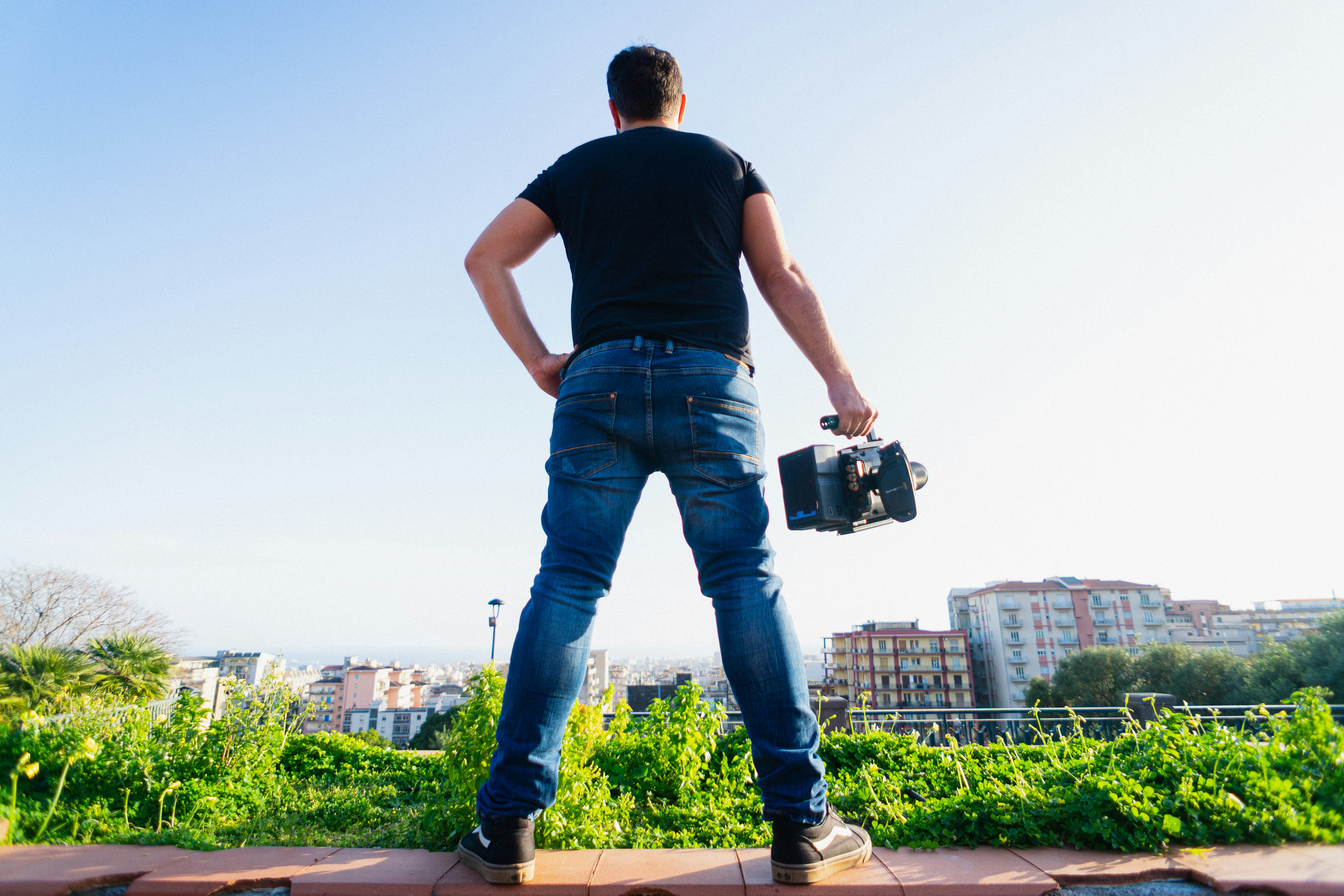 man in black t-shirt and blue denim jeans holding black camera