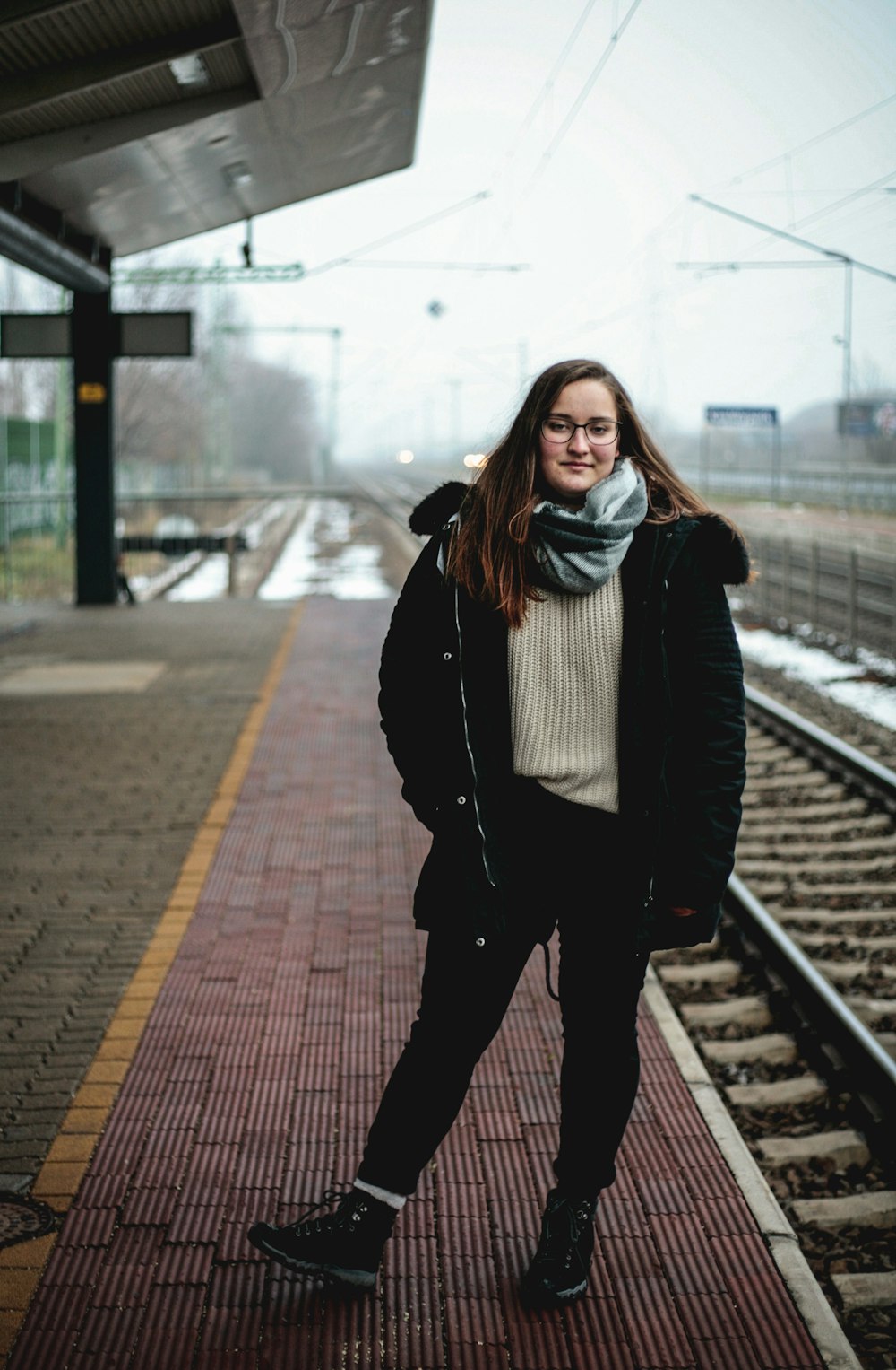 woman in black jacket standing on train rail during daytime