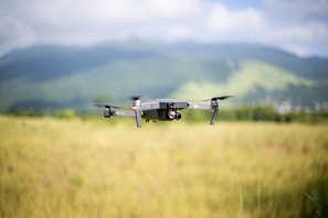 A drone captured mid-flight over a green field with mountains in the background