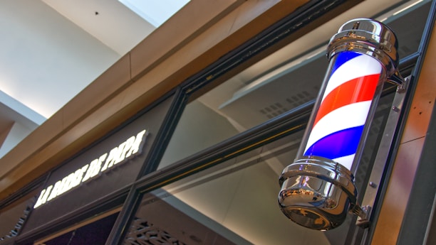 Close-up shot of a classic barber pole in monochrome tones outside the shop.