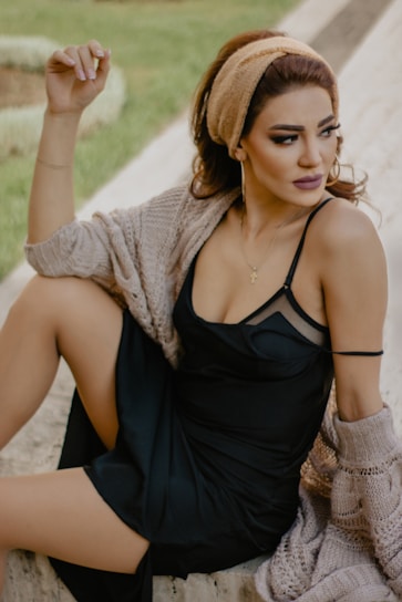 woman in black spaghetti strap dress sitting on brown wooden bench during daytime
