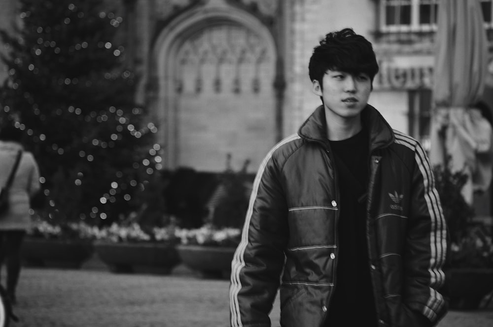 man in black leather jacket standing on the street in grayscale photography