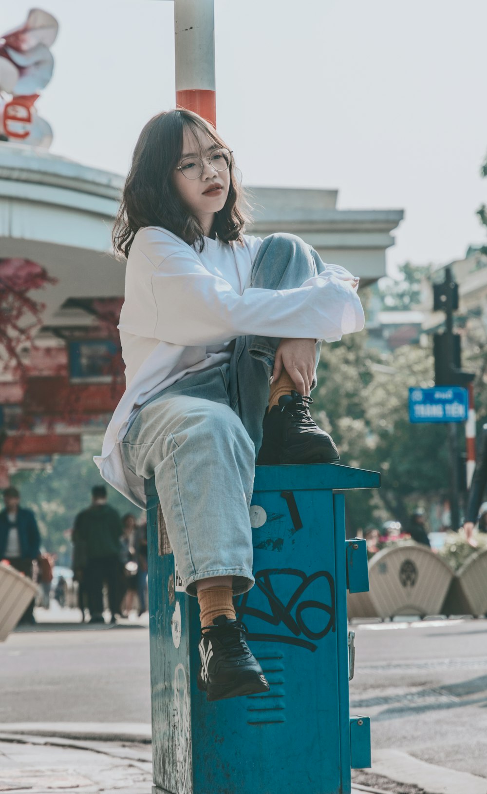 woman in white long sleeve shirt sitting on blue plastic trash bin during daytime